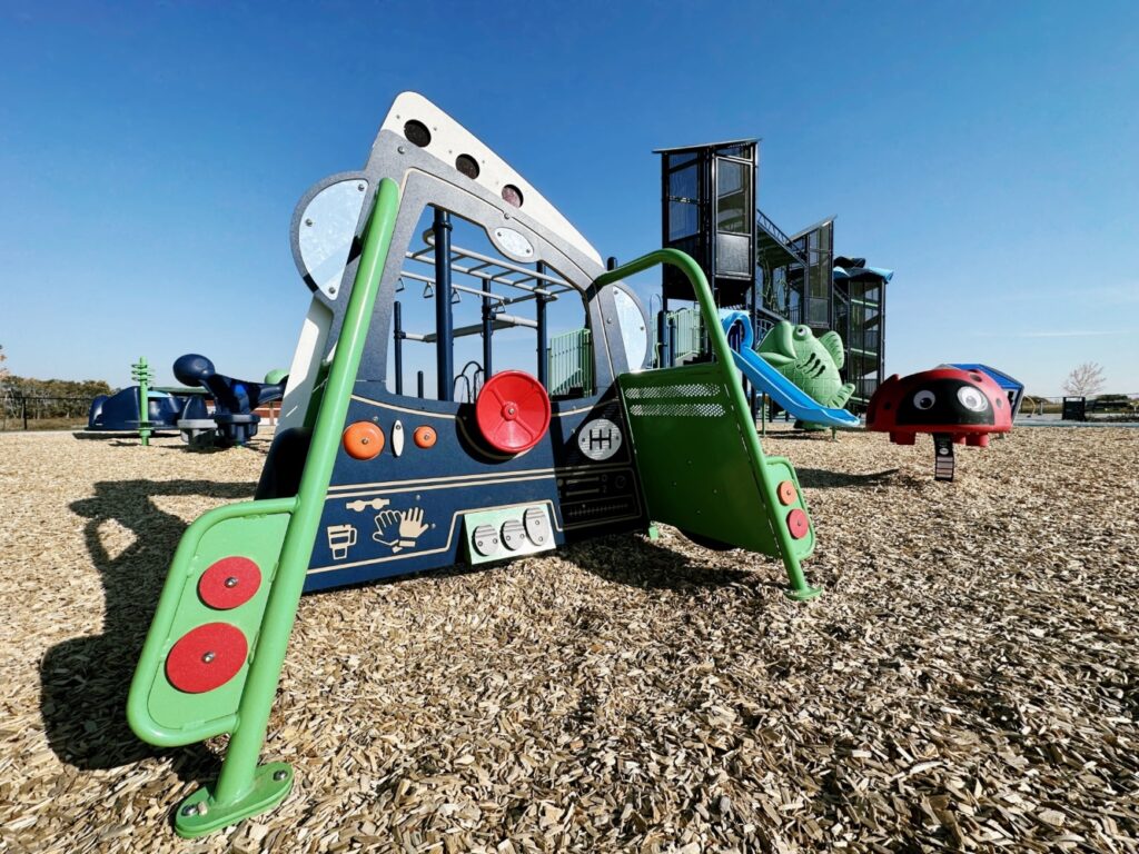 Pogadl Park-10 Close up view of Tot Builders Truck, Scarlet the Ladybug Spring Rider, Chameleon II Slide, Big Kahuna Climber, JAX Pack, Stand n Spin, and Bongo Steps.