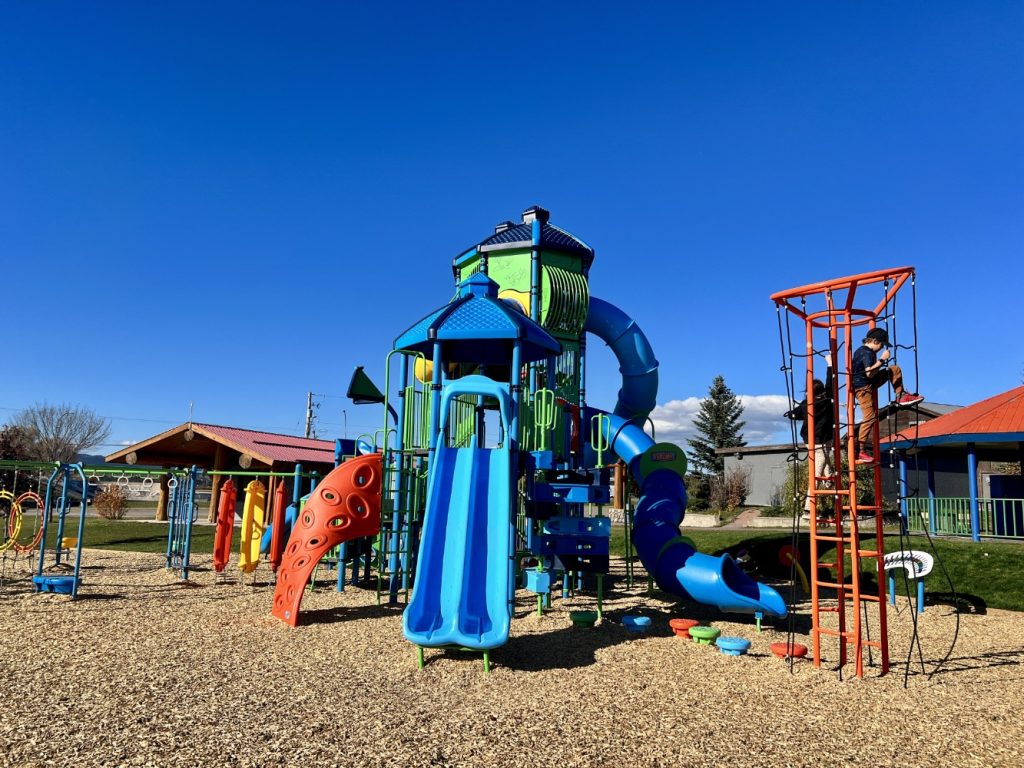 Radley Beach Playground-02 Colorful playground under clear blue sky featuring a large, multicolored slide structure and climbing equipment. A child climbs an orange tower, evoking joy.