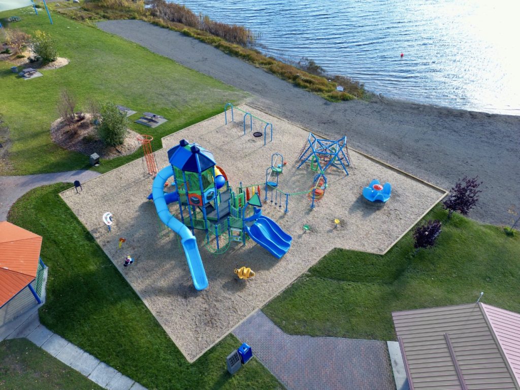 Radley Beach Playground-12 A vibrant playground near a lake, featuring slides, swings, and climbing structures. Surrounded by grass and pathways, it conveys a cheerful and inviting atmosphere.