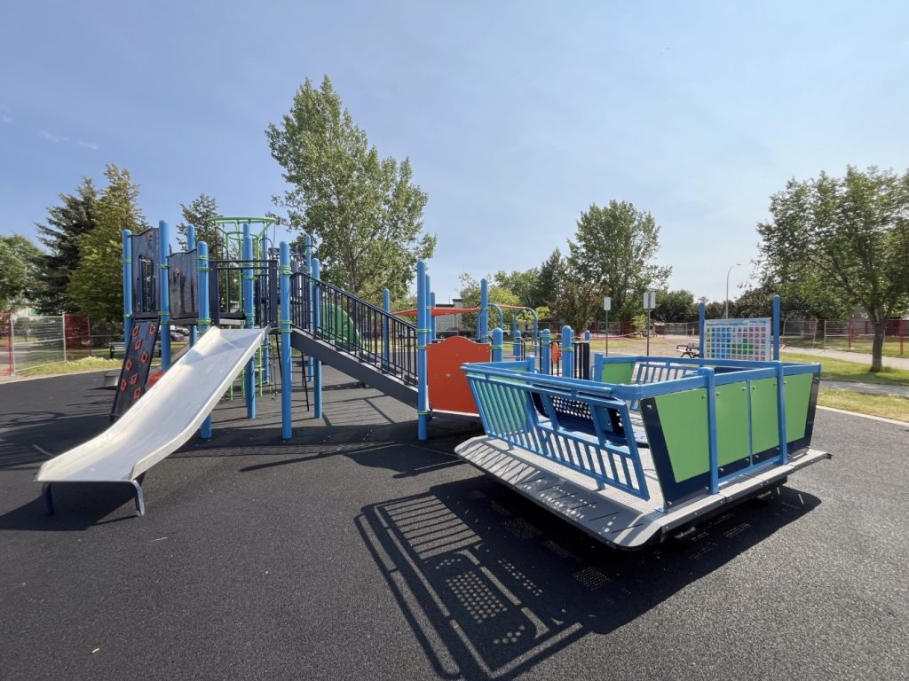 Chinook Lake Park-03 Playground at Chinook Lake Park with blue and green equipment under a clear sky. Features slides, climbing structures, and trees in the background, conveying a cheerful atmosphere.