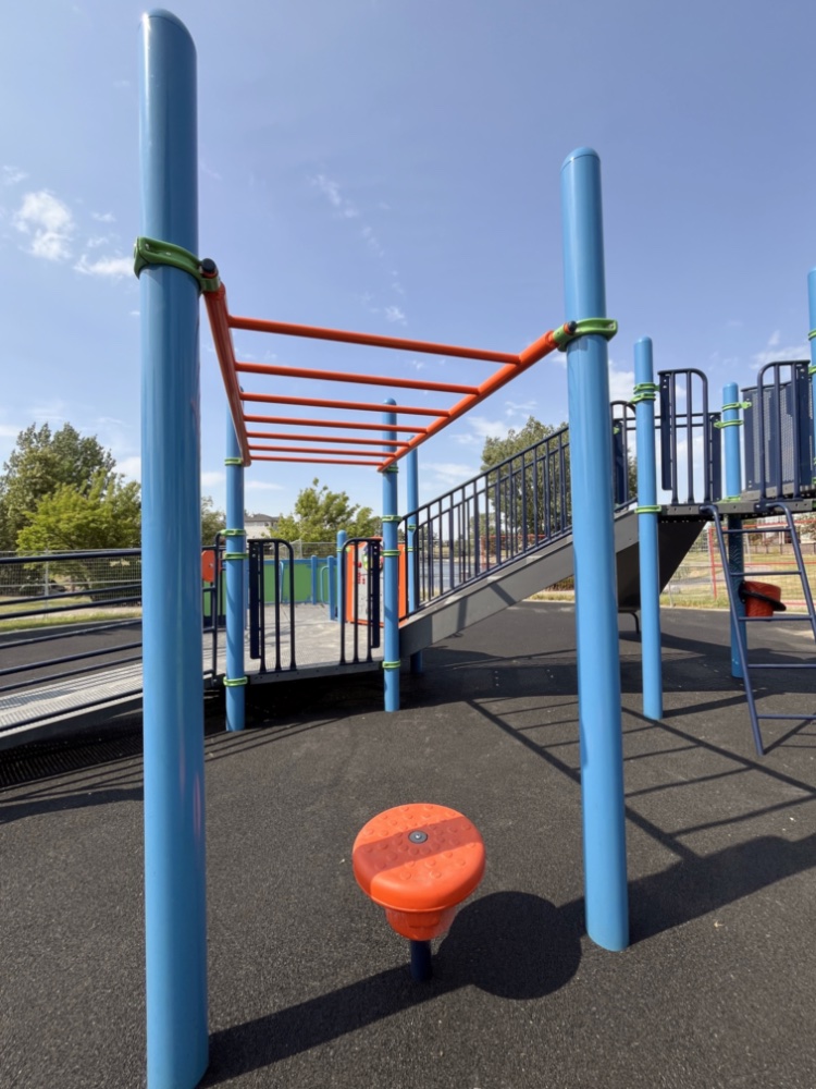 Chinook Lake Park-10 Playground with blue and orange monkey bars and a small orange step, set against a clear blue sky with trees in the background, conveys a playful atmosphere.