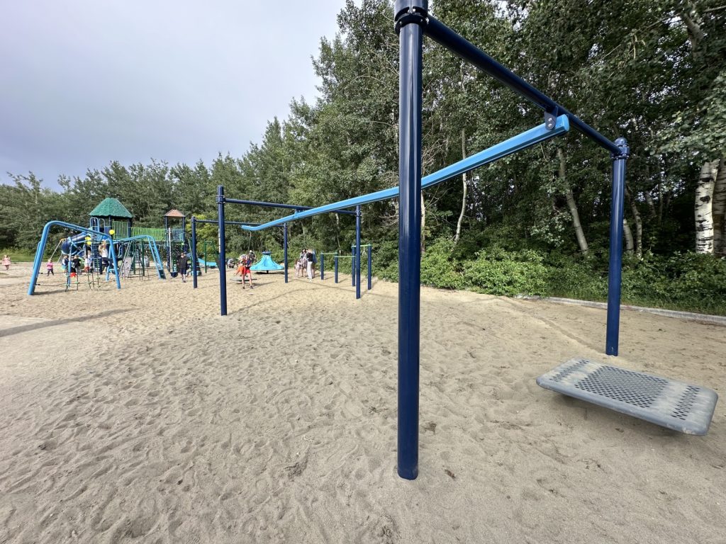 École Sacré Coeur-13 Playground at École Sacré Coeur with a blue zipline, surrounded by trees. Children are actively playing on the sandy ground, conveying a sense of joy and energy.