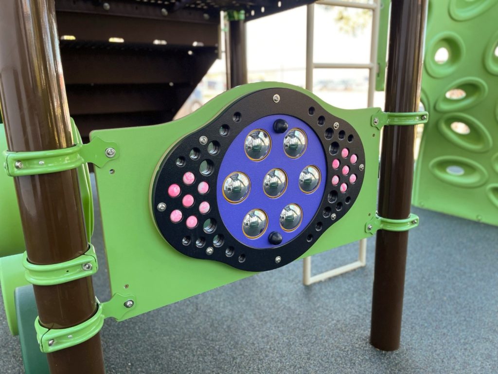 New Heights School-05 Close-up of a colorful playground panel at New Heights School with a mirror and rollerballs, framed by green and brown poles, creating an interactive, playful feel.