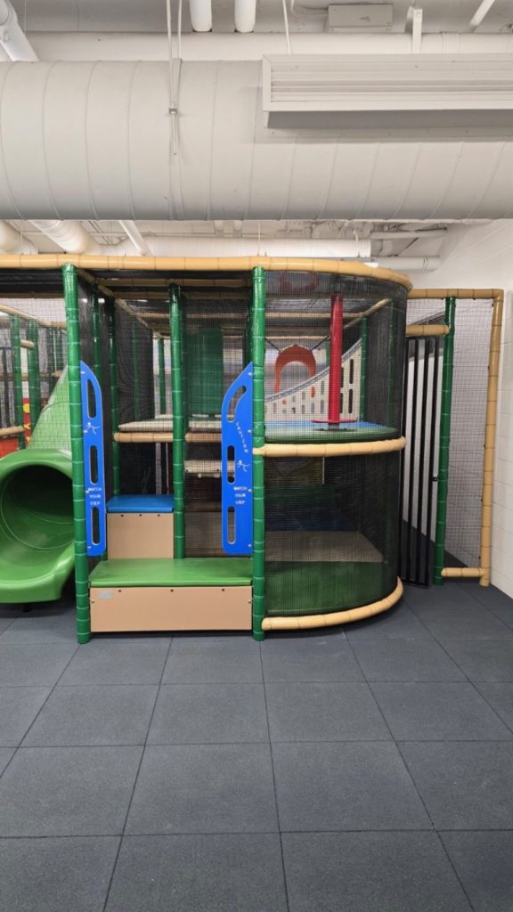 Village Square Leisure Centre-05 Indoor playground at Village Square Leisure Centre with green and blue play structures, including slides and climbing areas. The space has a fun, adventurous atmosphere.