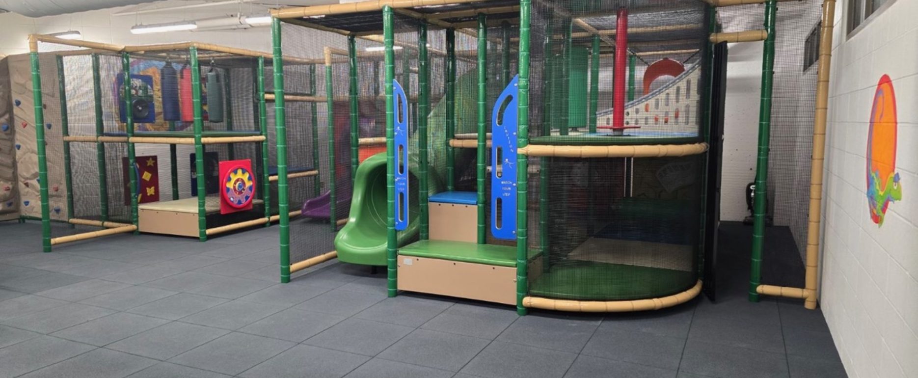 Indoor playground with colorful slides, climbing structures, and padded flooring. The space feels safe and inviting, designed for children's play.