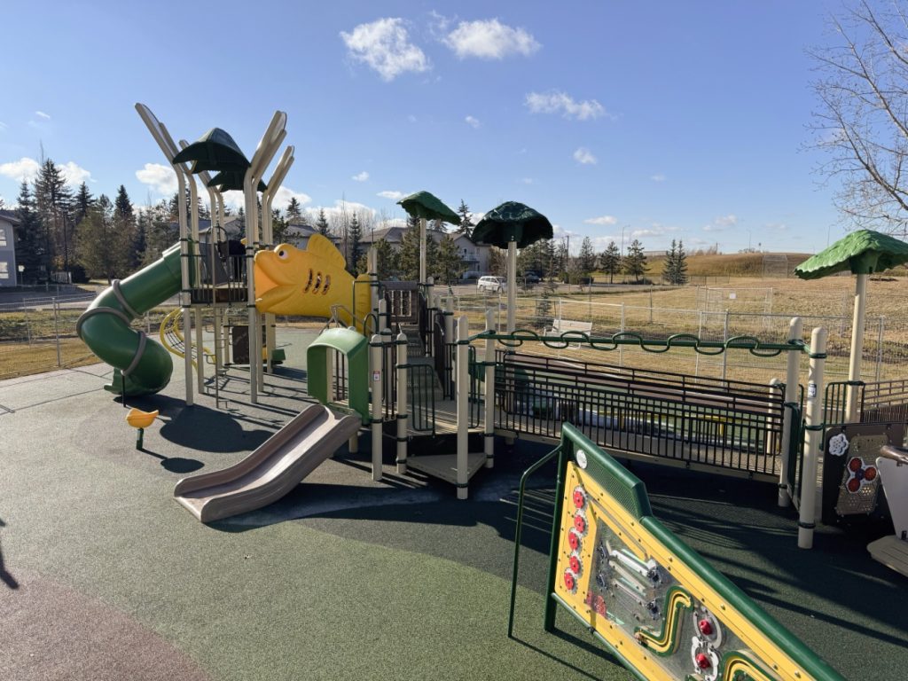 Willow Park School-01 Playground at Willow Park School with colorful slides, climbing structures, and a green spiral tube slide. Sunny day, clear blue sky, and trees in the background.