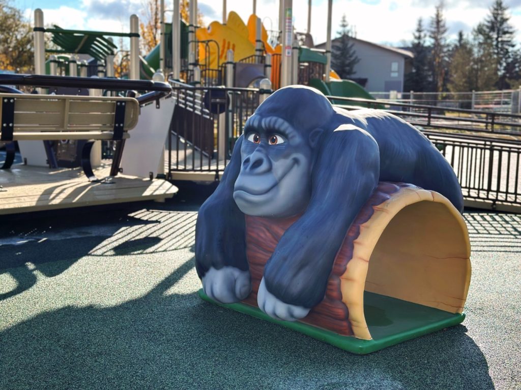 Willow Park School-02 Playful gorilla sculpture in a sunny playground, showcasing vibrant blues and greens. It rests on a log structure, creating a welcoming atmosphere.