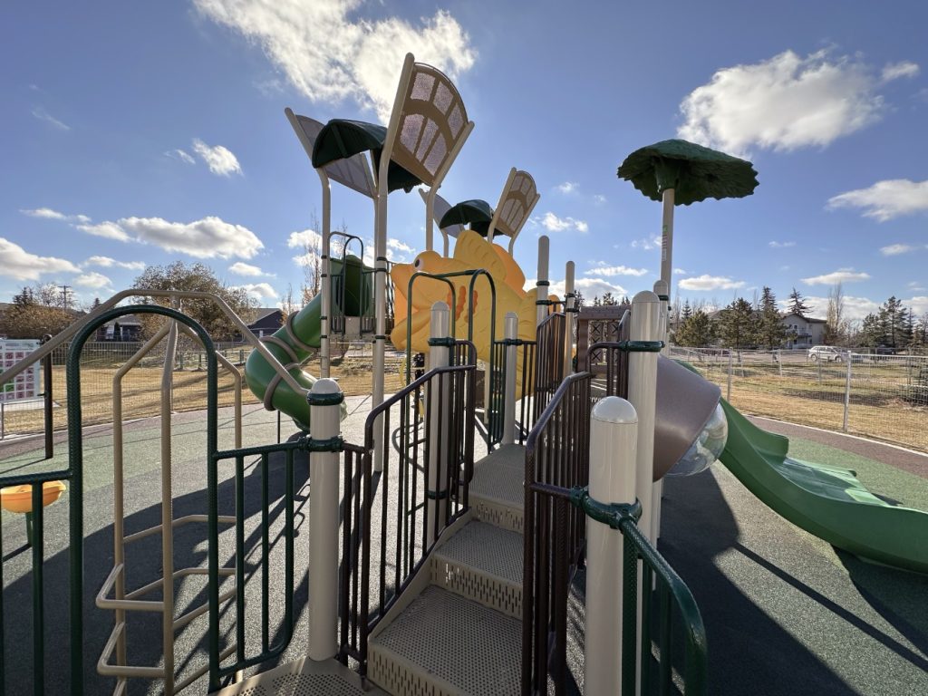 Willow Park School-10 Playground under a sunny sky with clouds. Features include slides, climbing structures, and tree-like shades, creating a vibrant and inviting atmosphere.
