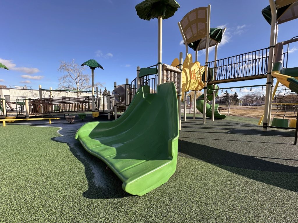 Willow Park School-11 Playground at Willow Park School with green slides, yellow climbing features, and a bridge. Sunny day, blue sky, and sparse trees in the background suggest a lively atmosphere.