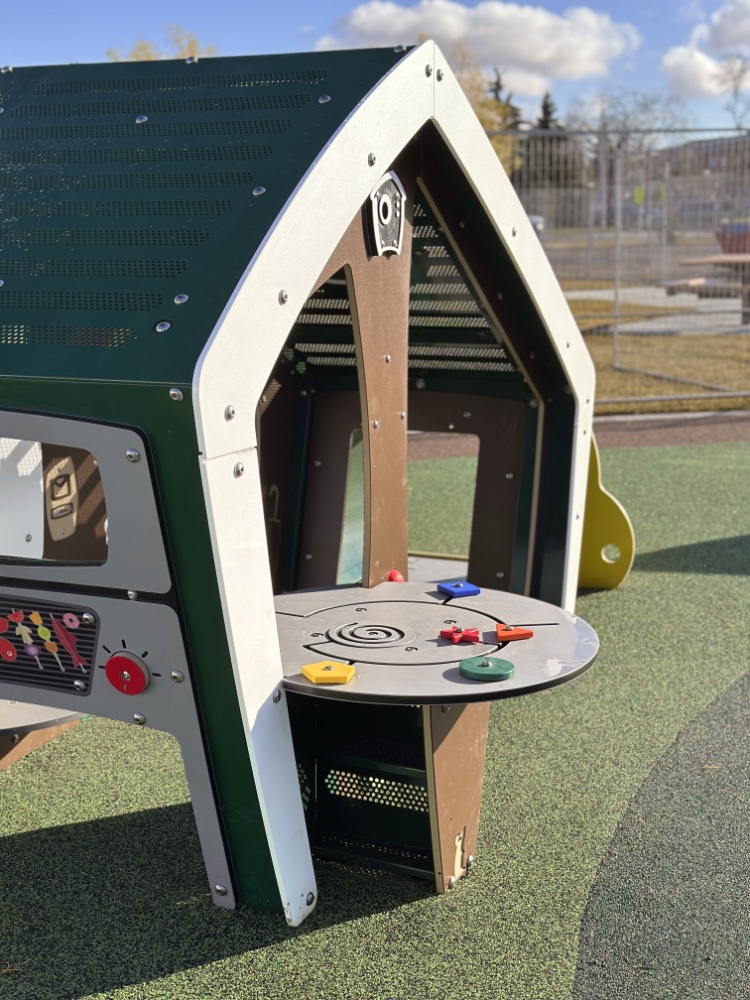 Willow Park School-16 A colorful playground structure resembling a small house with a table featuring various geometric shapes. It sits on a sunny day, exuding a cheerful vibe.