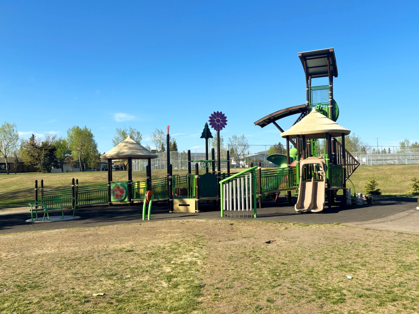 Kin Park-01 Kin Park playground in Dawson Creek, BC, with thatched-style roofs, a tall tower and an inclusive merry-go-round.