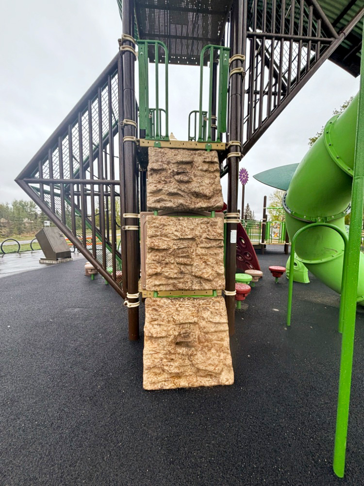 Kin Park-10 Rock climbing wall panels leading up the tower, with a green tube slide and stepping pods on black rubber.