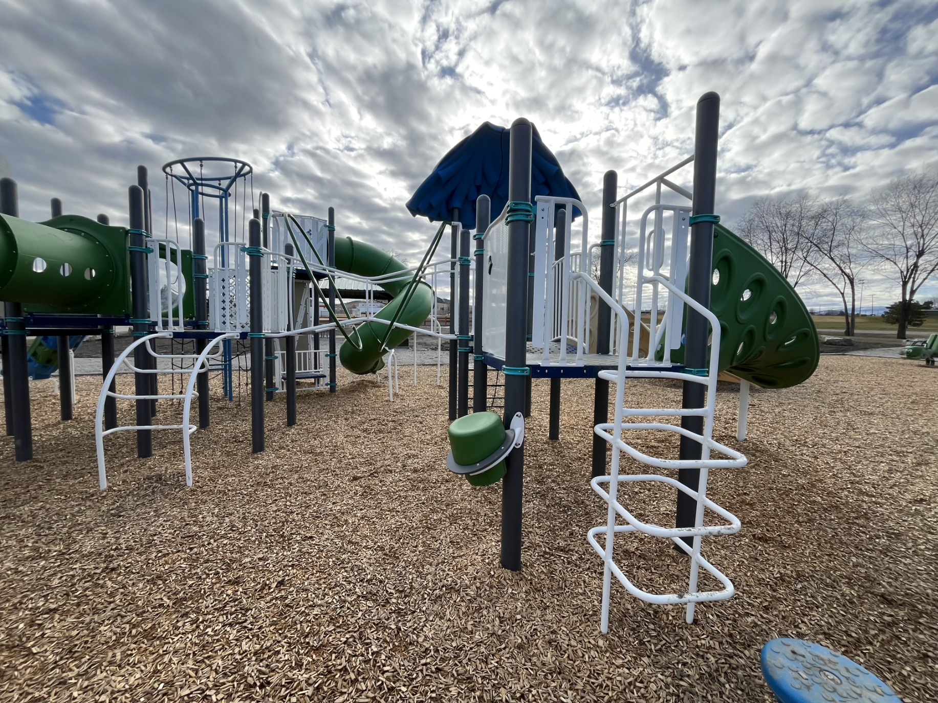 White ladders, a green bongo drum and a green tube slide on wood chip surfacing.