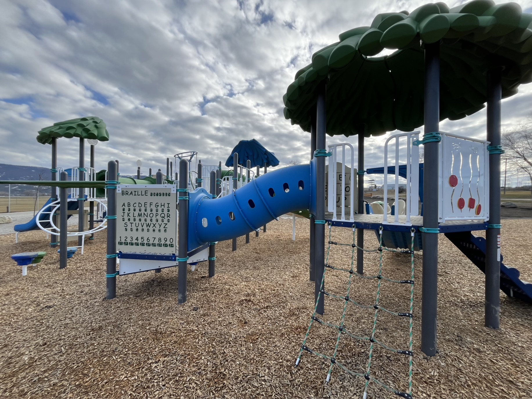 Braille panel, blue crawl tunnel and rope net ladder beneath a green leaf canopy roof.