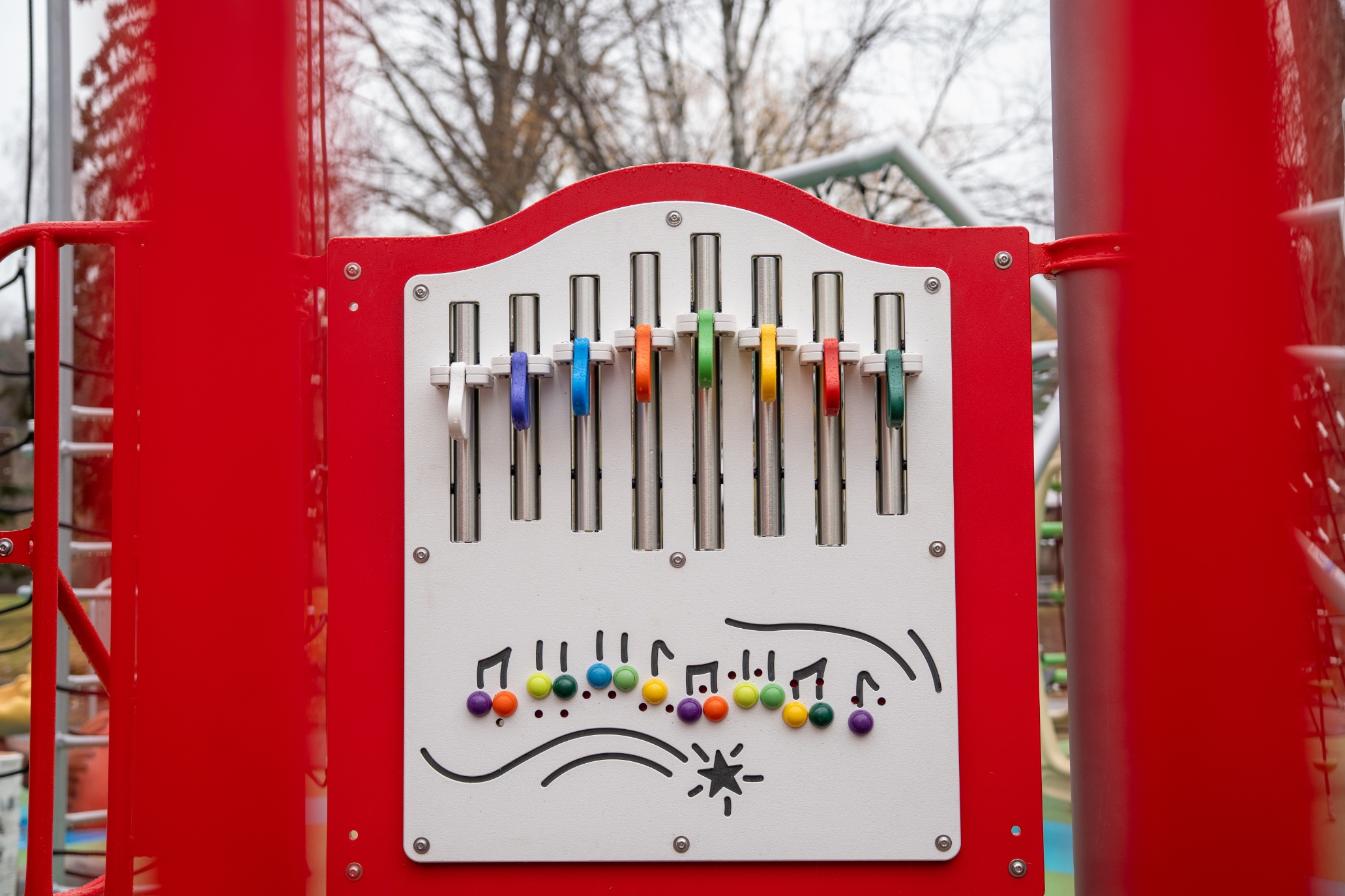 Musical chime panel with eight colourful mallets and a song chart, framed by red posts.