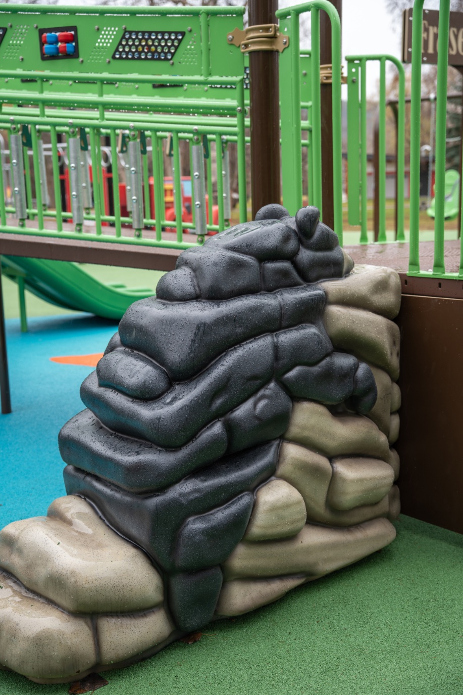 Black and grey bear climber sculpture beside a green railing lined with metal chimes.