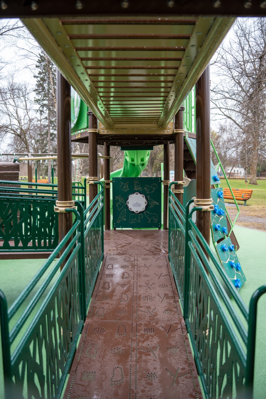 Ramp with tactile footprints leading to a wildlife panel, a blue-grip climbing wall alongside.