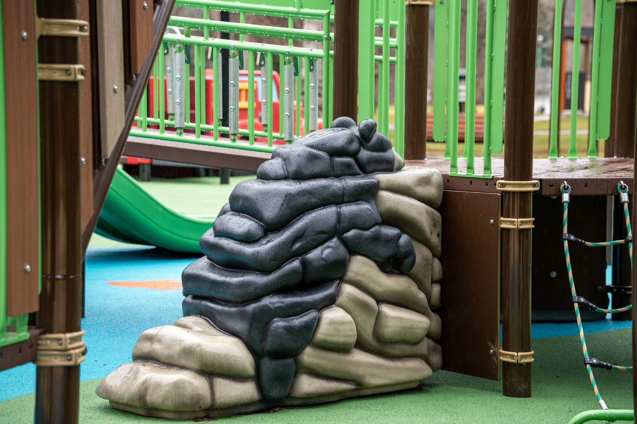 Bear climber sculpture at the base of the play deck, with a rope ladder and green slide nearby,