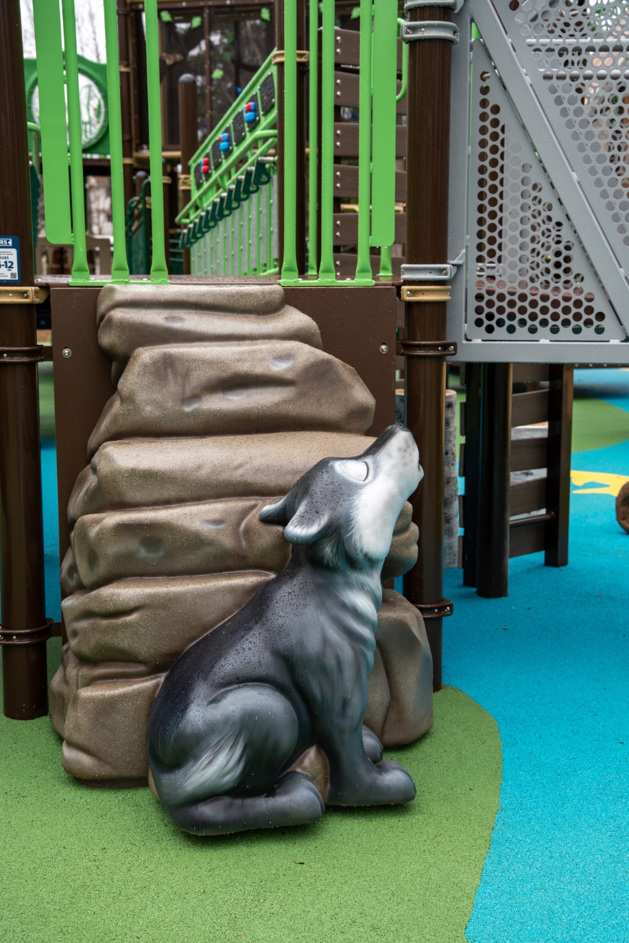 Howling wolf sculpture against a rock climber on blue and green rubber surfacing.