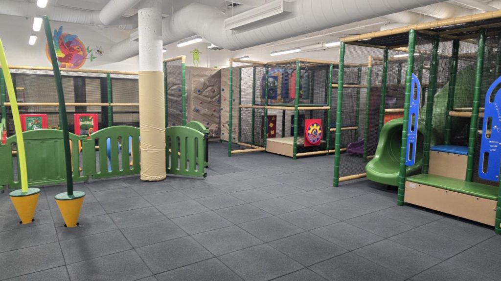Village Square Leisure Centre-02 Indoor playground with colorful slides, climbing walls, and padded flooring. Green and yellow structures create a vibrant, fun atmosphere.