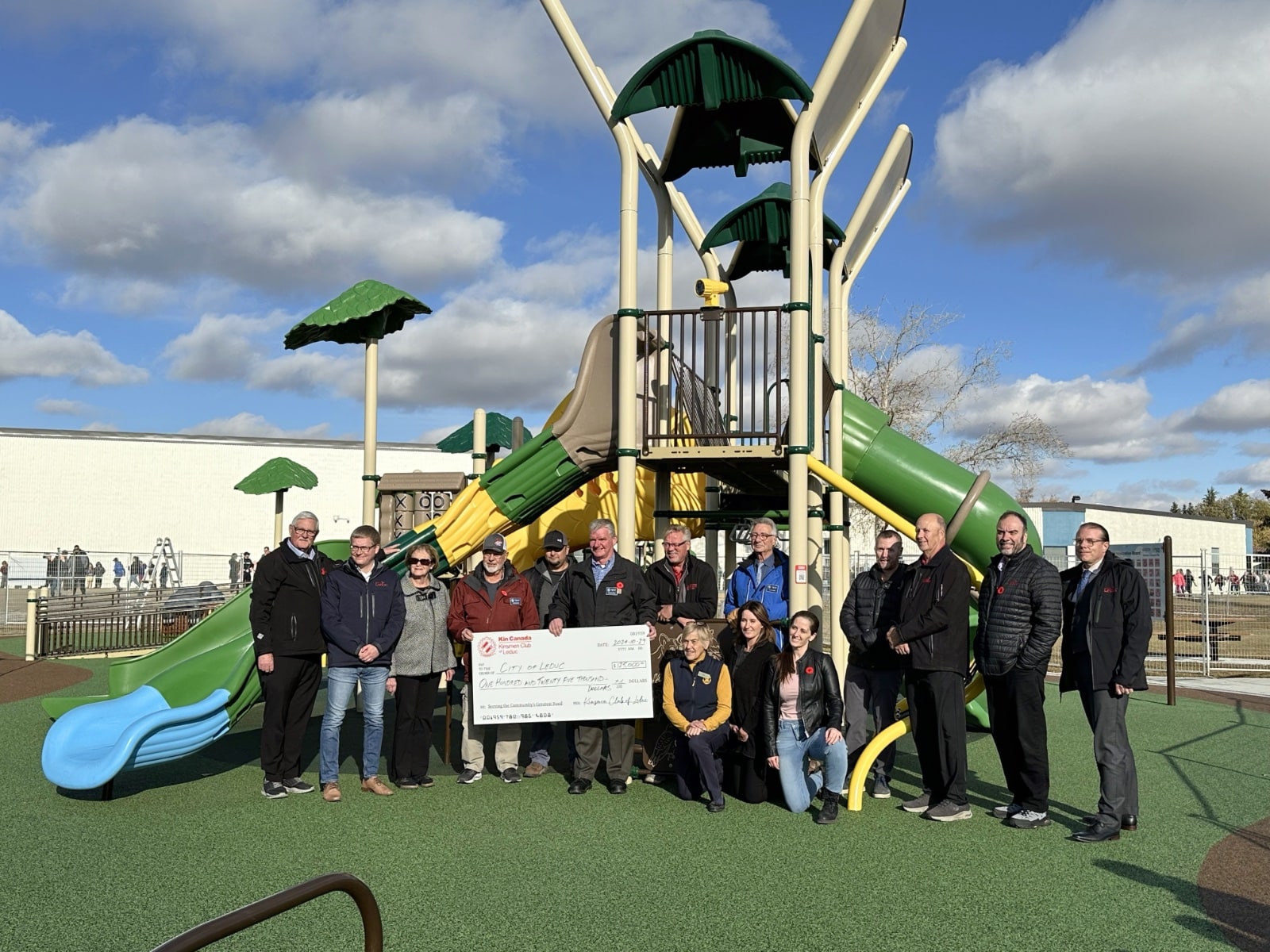 Group photo in front of a green and yellow play tower, holding a ceremonial donation cheque.