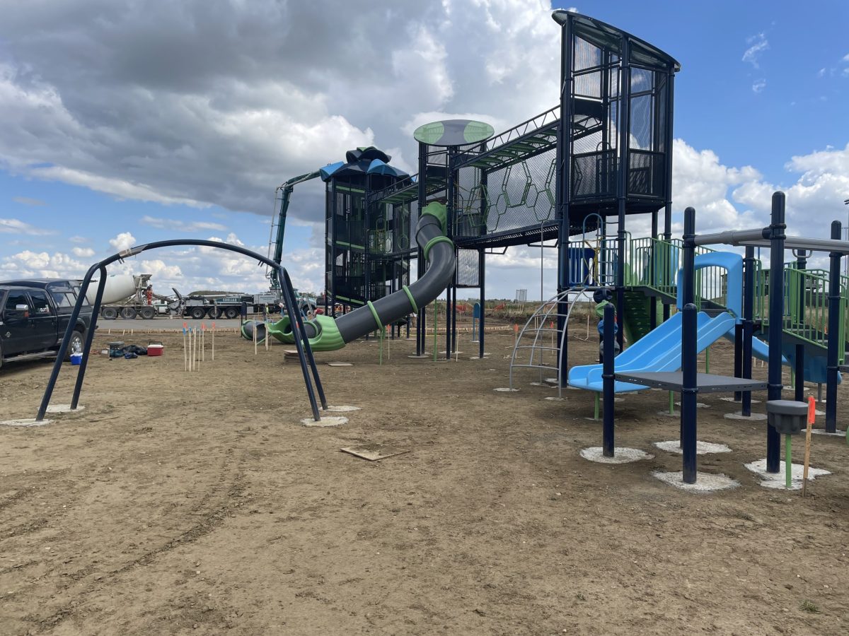 A commercial playground design being installed on a bare dirt site with a concrete truck in the background.