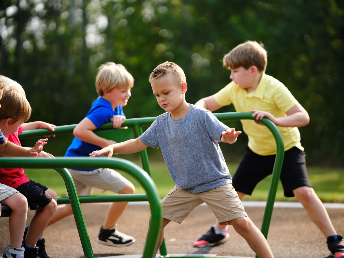 Children playing on a green merry-go-round at the playground.