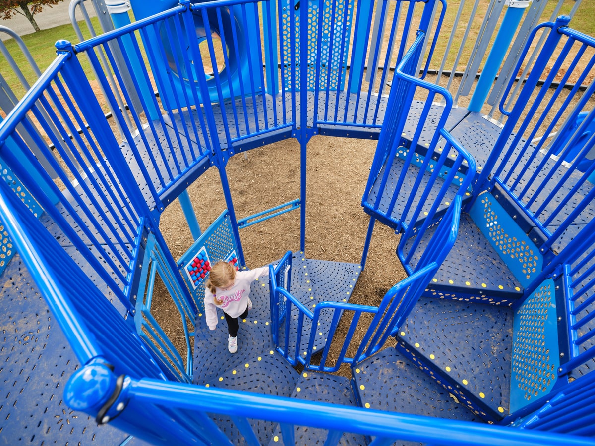 Aerial view looking down a blue spiral staircase on a play tower, with a child climbing up.