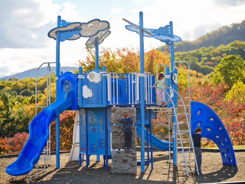 Blue play tower with cloud panels and a rock climbing wall, showing features that affect commercial playground cost.