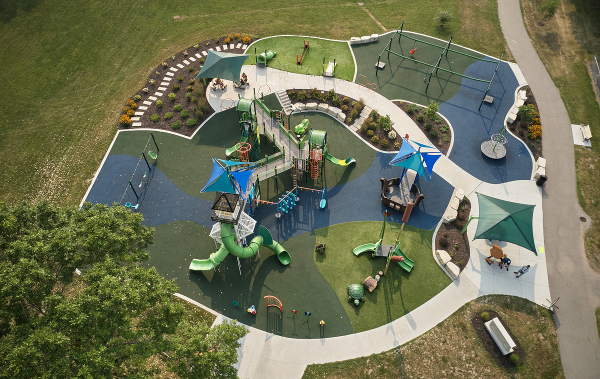Aerial view of a curved commercial playground design with green and blue rubber surfacing, shade sails and paths.