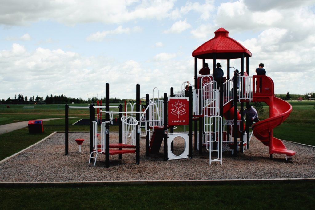 Red and white Canada 150 commercial playground design with a spiral slide on a wood chip surface.