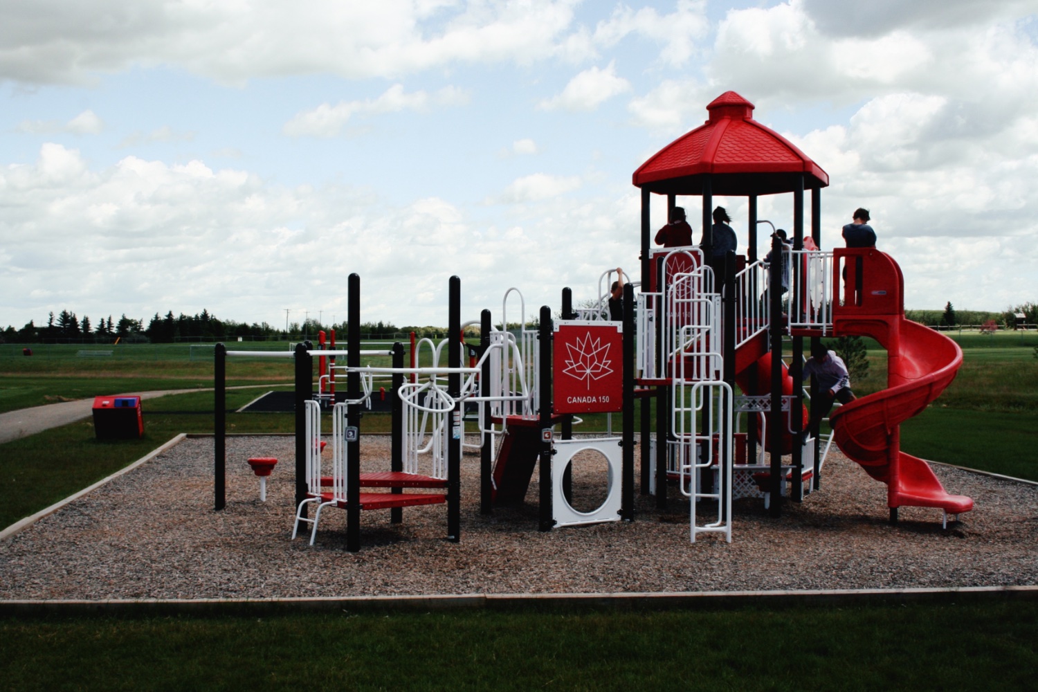 Red and white Canada 150 commercial playground design with a spiral slide on a wood chip surface.