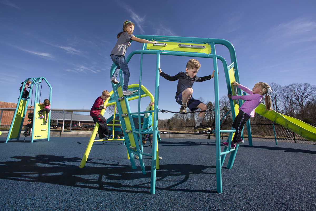 Five children climbing a teal and lime green playground climber on blue rubber safety surfacing.