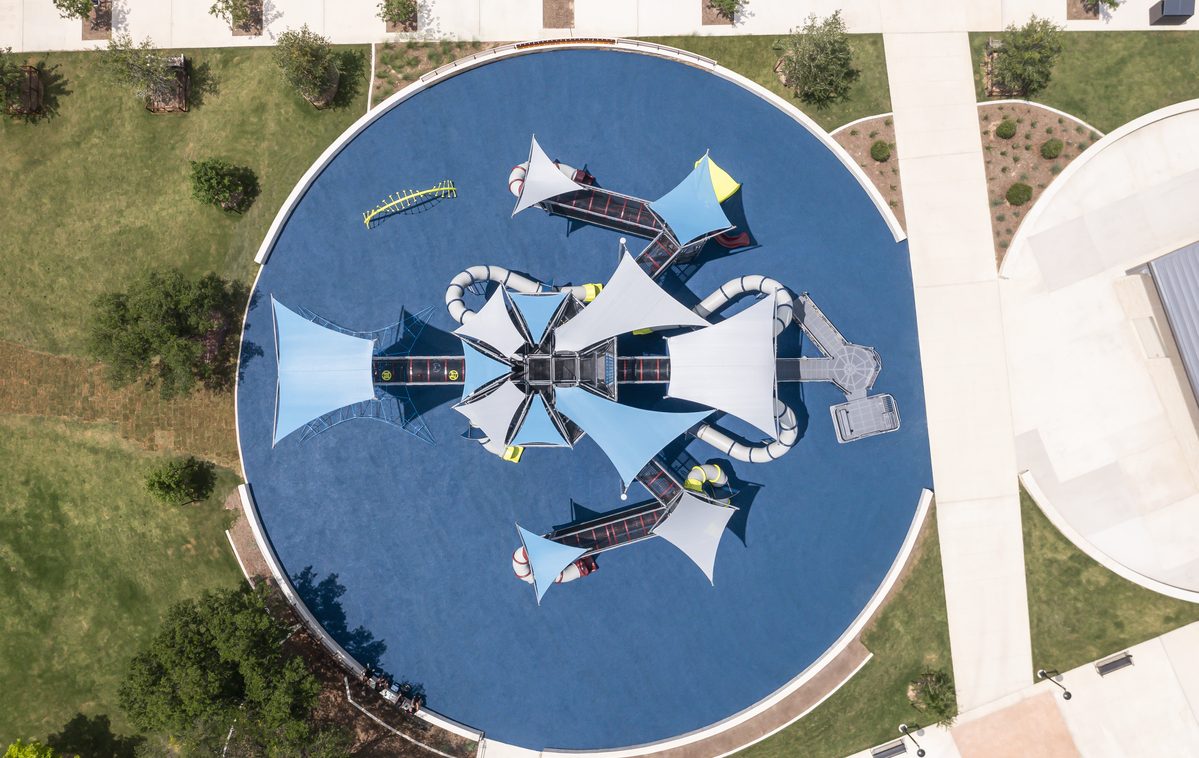 Overhead view of a circular commercial playground design with white shade sails on blue poured rubber.