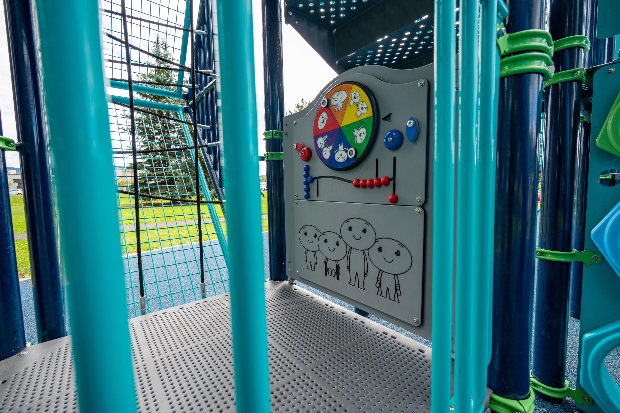 Colourful spinner and bead play panel on the deck of a play structure beside a cable net climber.