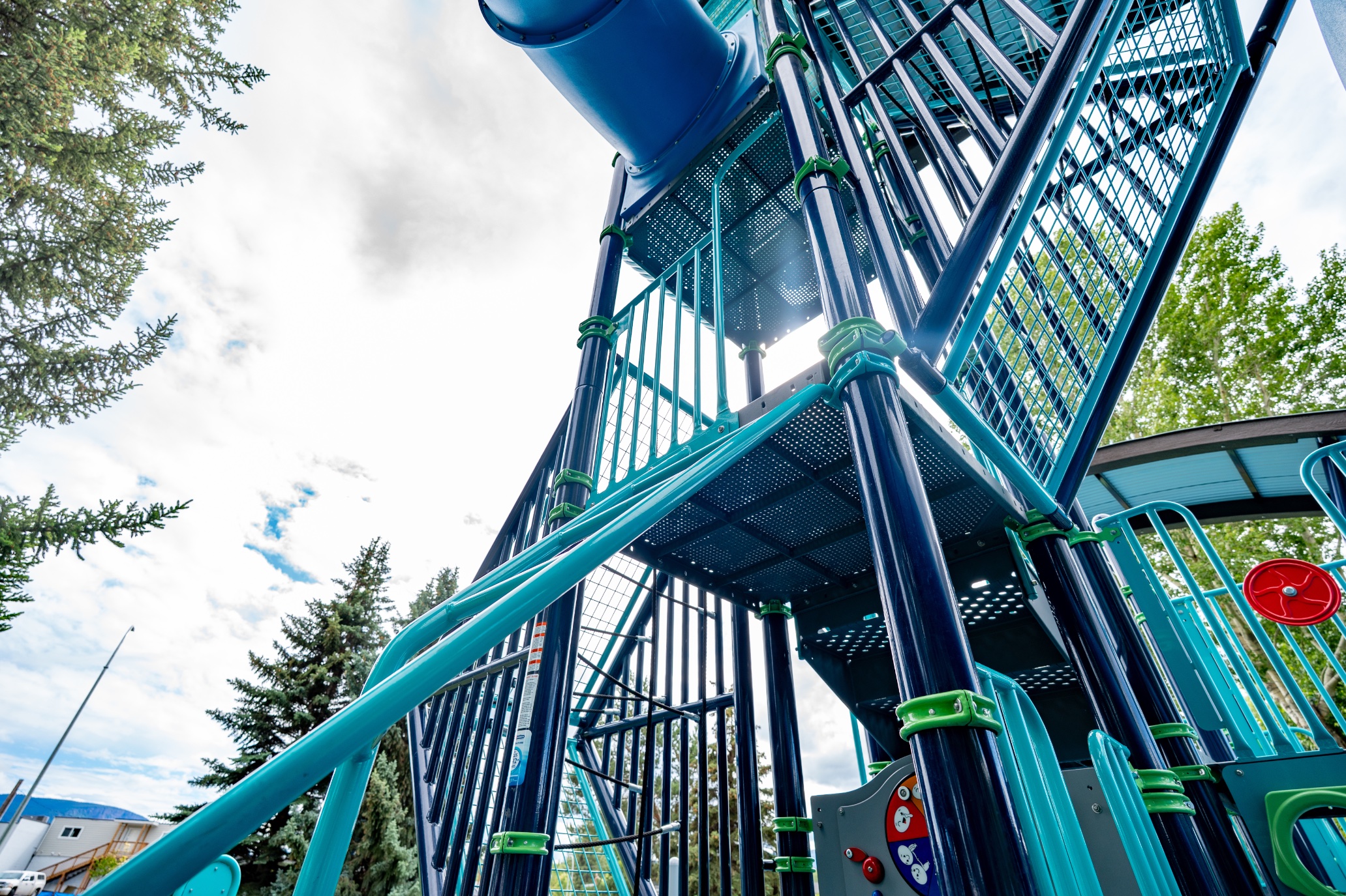 Looking up at the multi-level tower decks, teal railings and blue tube slide of a play structure.