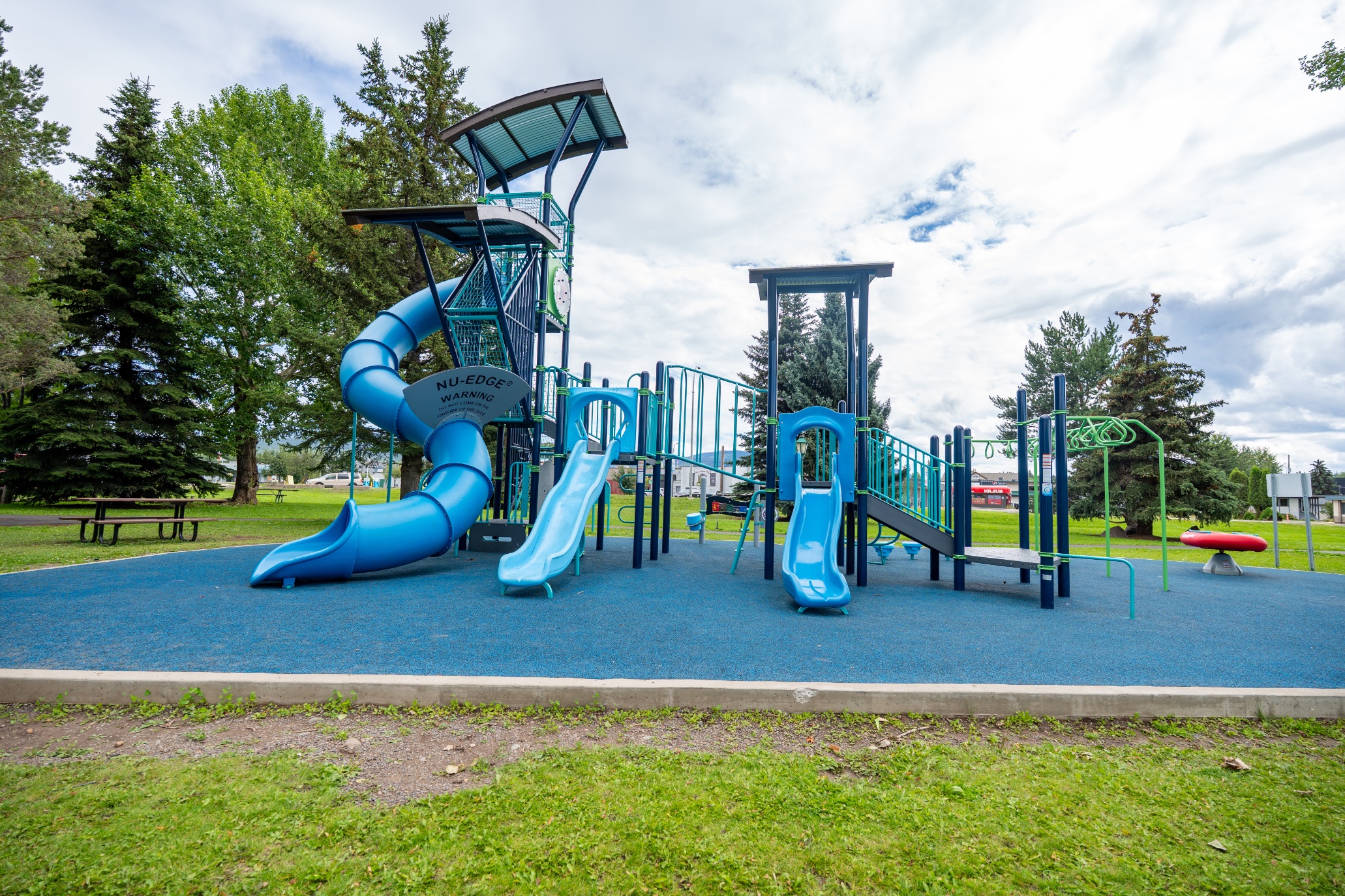 Side view of the play structure with a spiral tube slide, two wave slides and stairs for access.