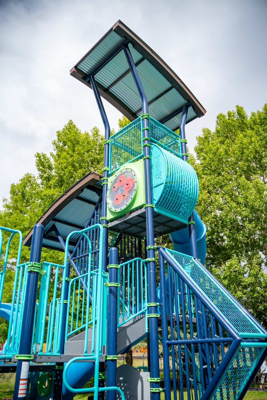 Tall play tower with shade canopies, a teal tunnel and a green gear panel against the sky.