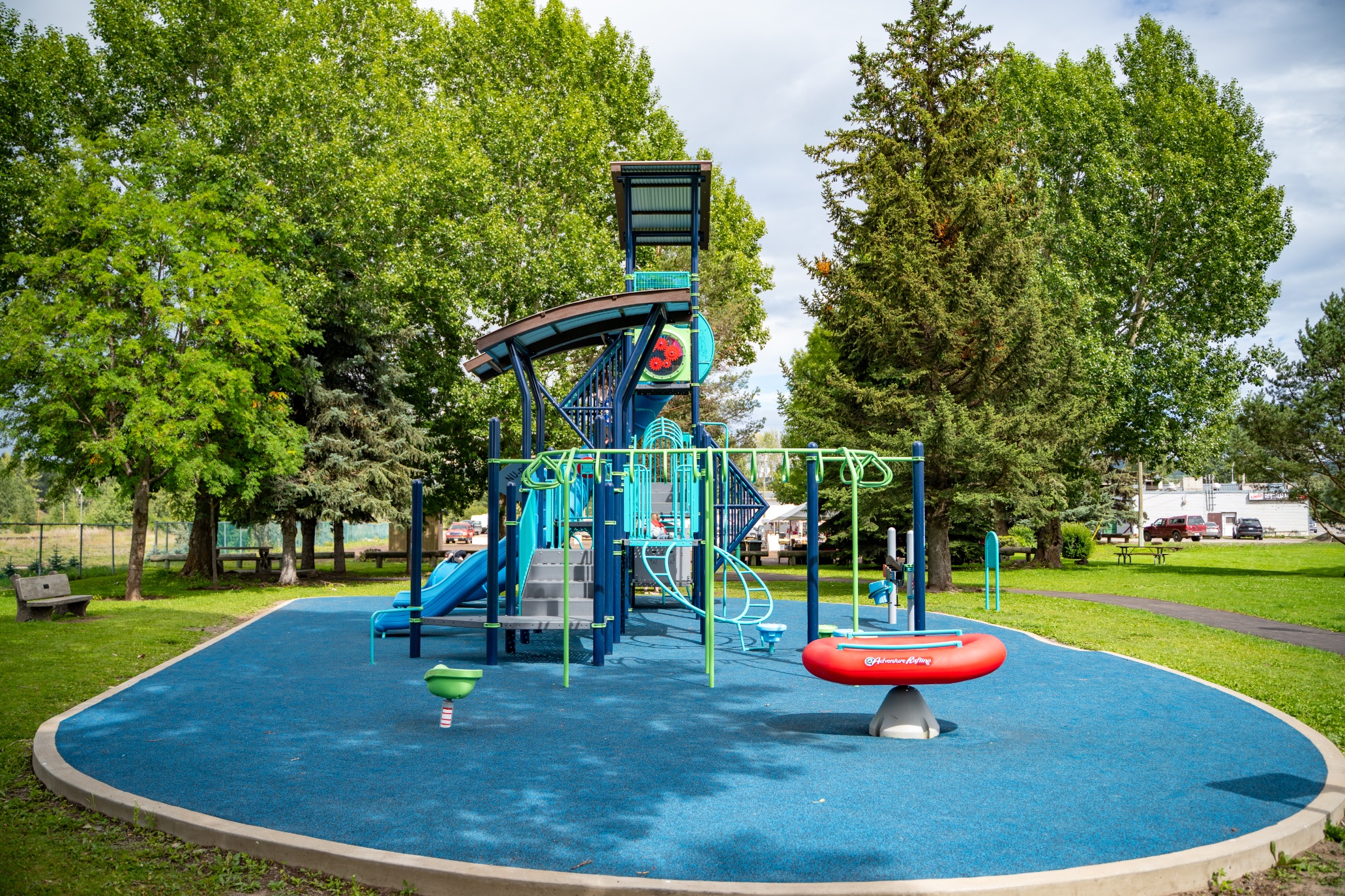 The playground at Steelhead Park in Houston, BC, with a green loop climber and red raft see-saw.