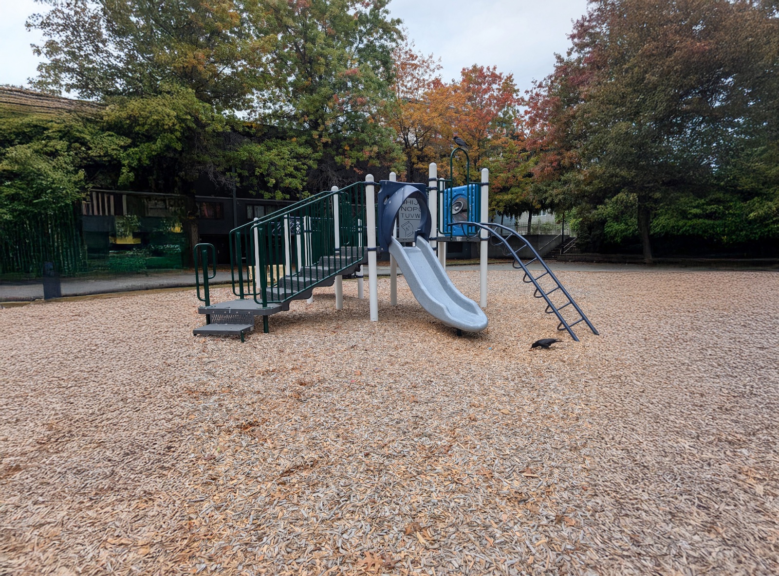 Grey slide, curved ladder and alphabet panel on the wood chip playground at MacLean Park in Vancouver, BC.