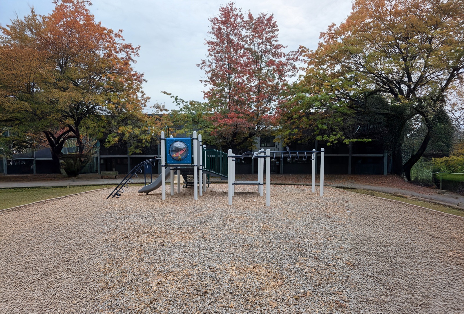 Wide view of the play structure's monkey bars and tower beneath colourful autumn trees at MacLean Park in Vancouver, BC.