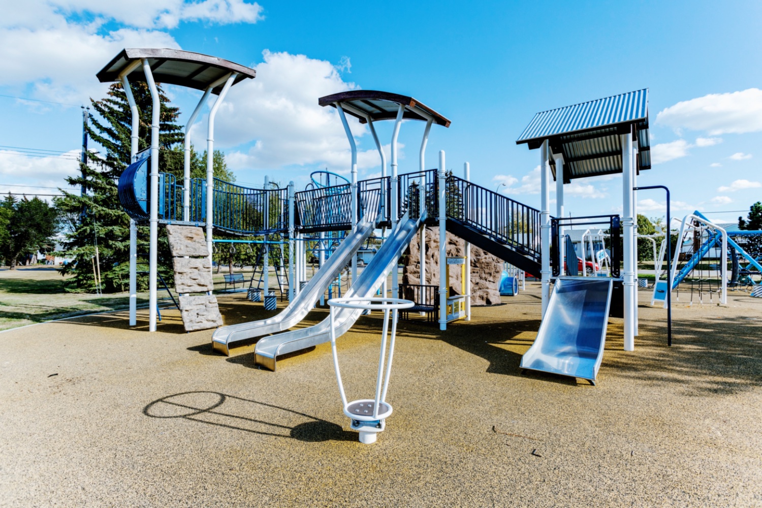 White and blue play structure with steel slides, rock climbing walls and a standing spinner.