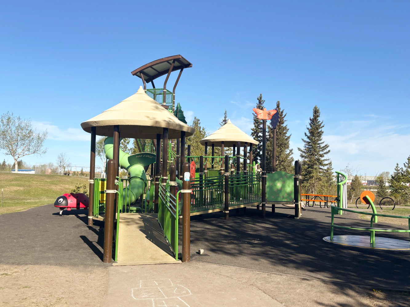 Green play structure with canopy roofs, an accessible ramp, tube slide and butterfly topper.