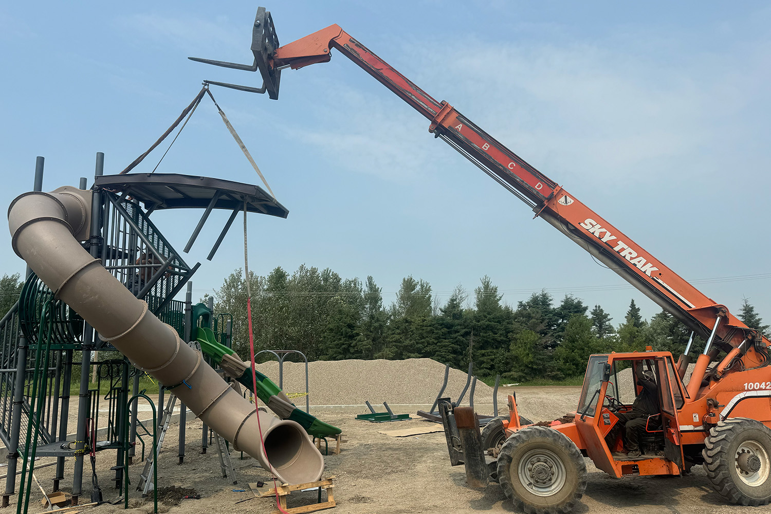 A crane lifting a canopy roof onto a play tower's tube slide during installation.