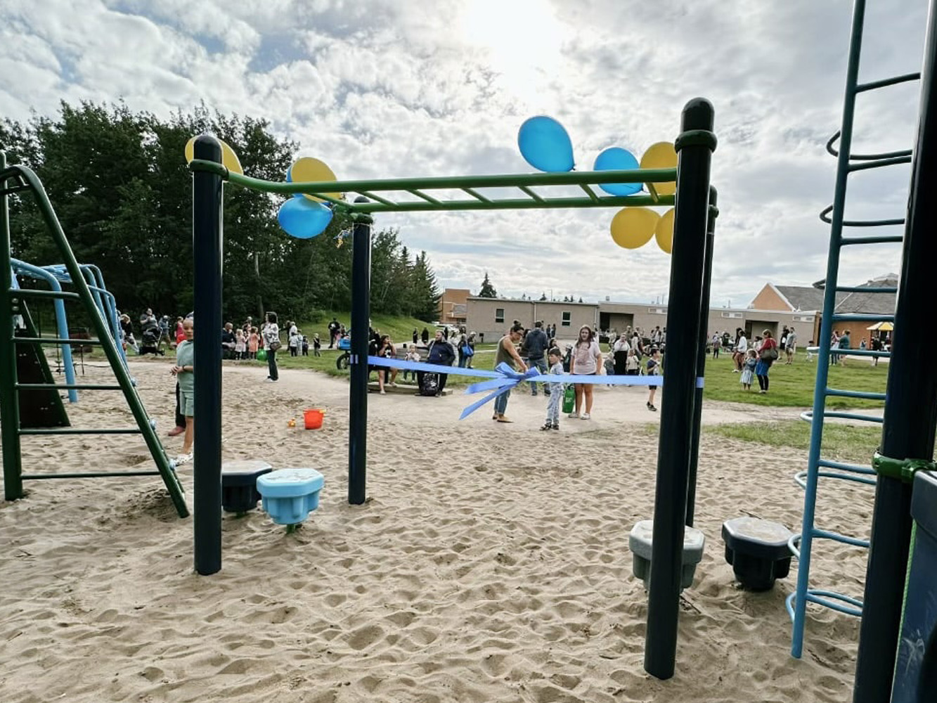 Children celebrating a ribbon-cutting at a new playground's monkey bars, decorated with balloons.