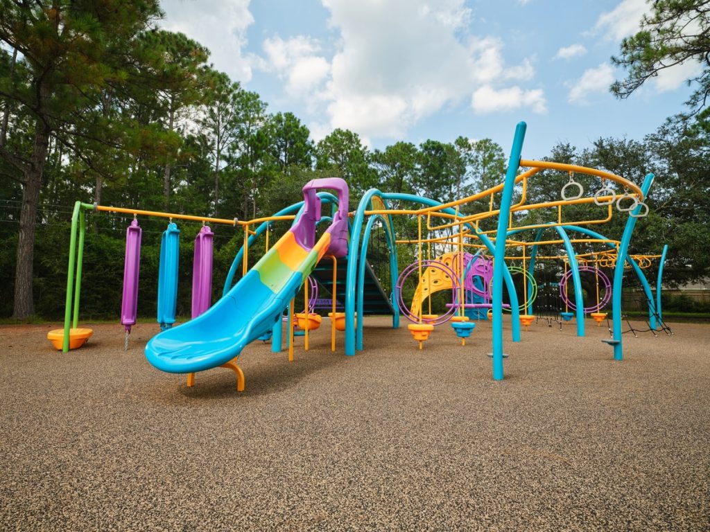 Colorful playground with purple, teal and orange structures, ring climbers and swings on tan rubber surfacing.