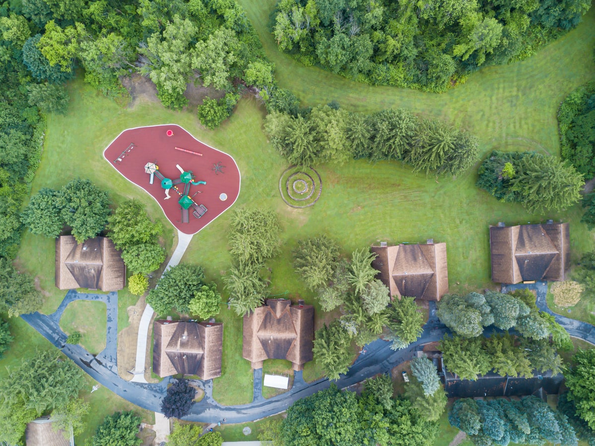 Aerial view of a small red rubber-surfaced playground tucked among townhouses and trees.