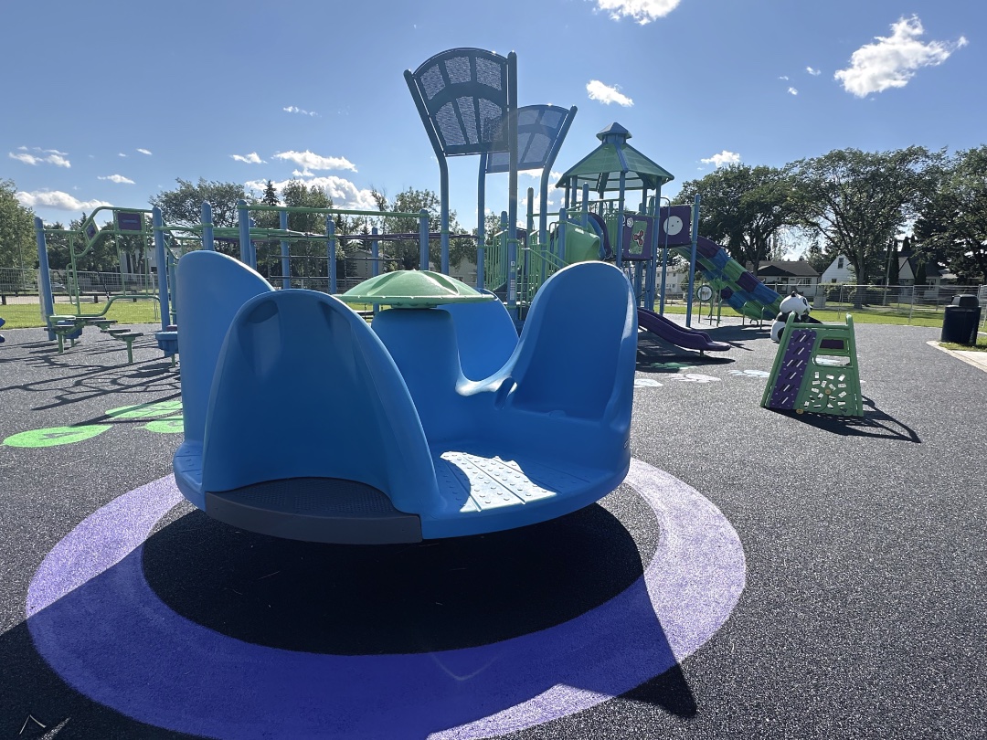 Blue merry-go-round on a painted purple circle, with a blue and green play structure behind.