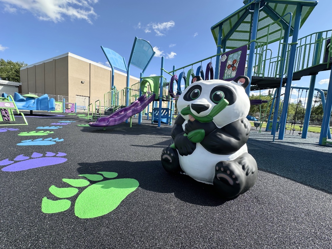 Panda sculpture on black rubber surfacing with painted paw prints and a purple slide behind.