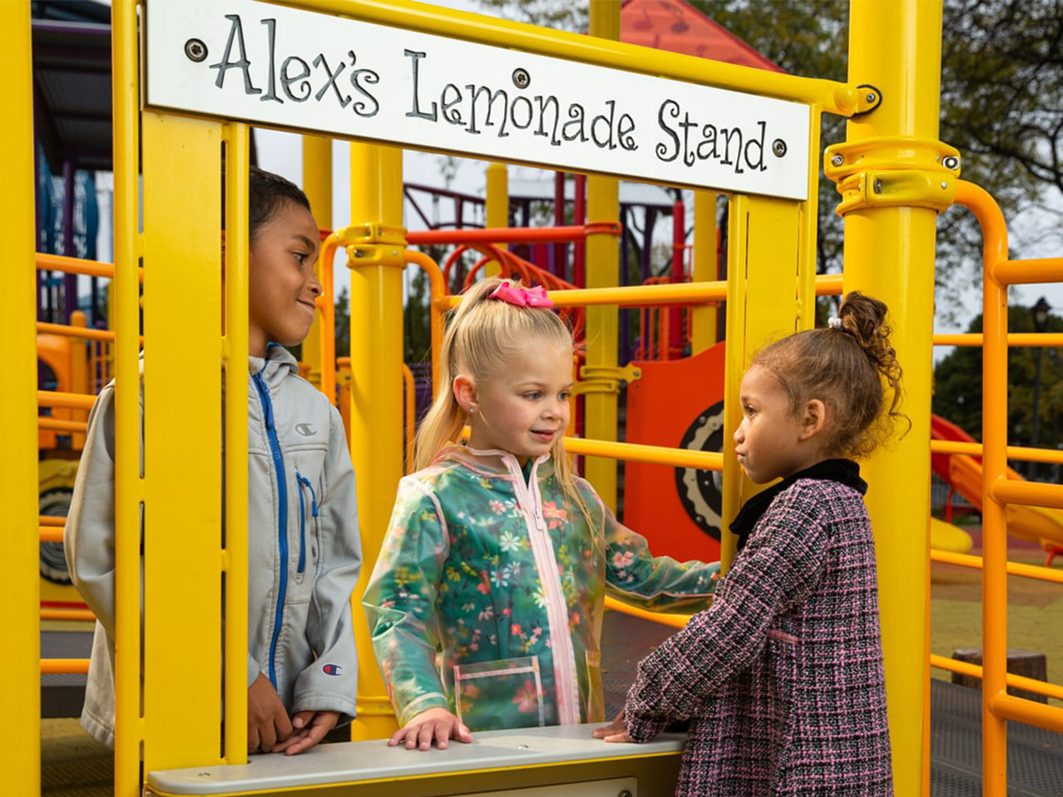 Alex's Lemonade Stand play panel where three children pretend to run a lemonade stand.